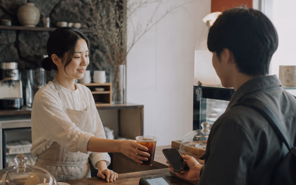 제주 카페 카운터에서 사장님이 음료를 건네고 젊은 중국인 여행자가 스마트폰으로 결제하는 순간
